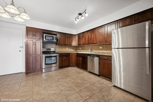 kitchen featuring appliances with stainless steel finishes, decorative light fixtures, sink, backsplash, and light stone counters