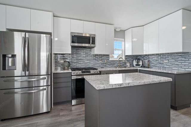 kitchen with stainless steel appliances, a sink, white cabinetry, light countertops, and a center island