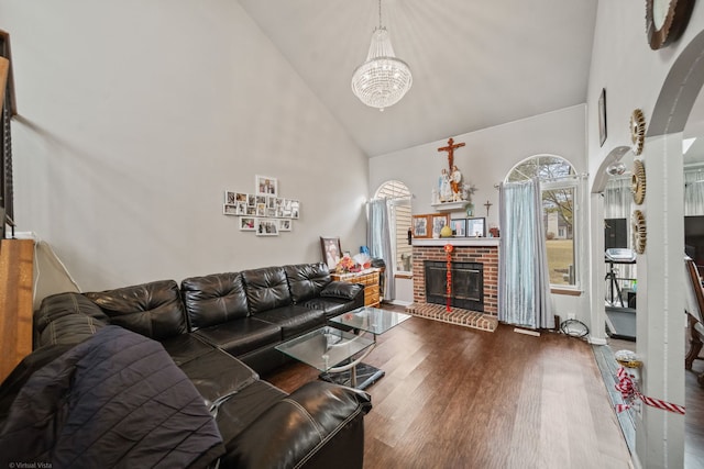 living room featuring hardwood / wood-style floors, high vaulted ceiling, a chandelier, and a brick fireplace