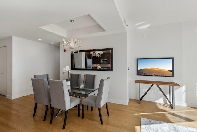 dining space with an inviting chandelier, a raised ceiling, and hardwood / wood-style floors