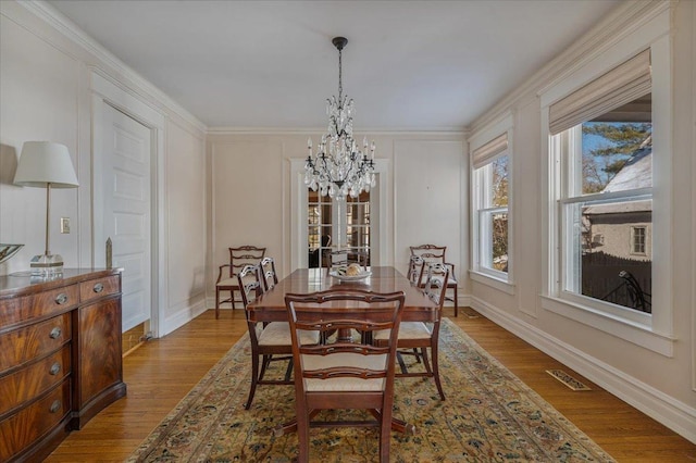 dining area featuring a chandelier, wood finished floors, visible vents, and a decorative wall