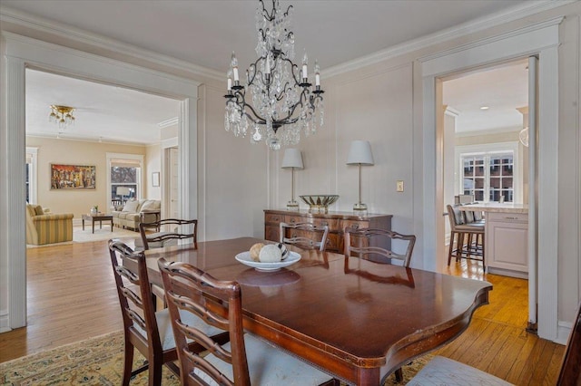 dining space with light wood-style floors, crown molding, and an inviting chandelier