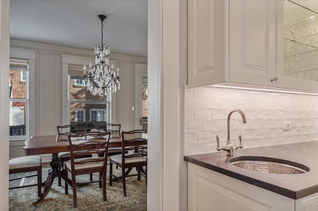 bar with a chandelier, backsplash, a sink, and decorative light fixtures