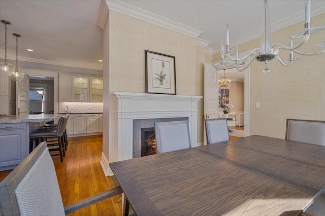 dining area with ornamental molding, wood finished floors, a lit fireplace, and an inviting chandelier