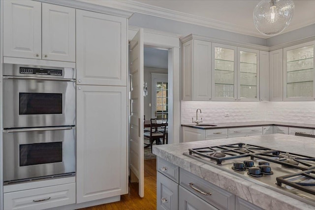 kitchen featuring crown molding, appliances with stainless steel finishes, glass insert cabinets, white cabinets, and a sink