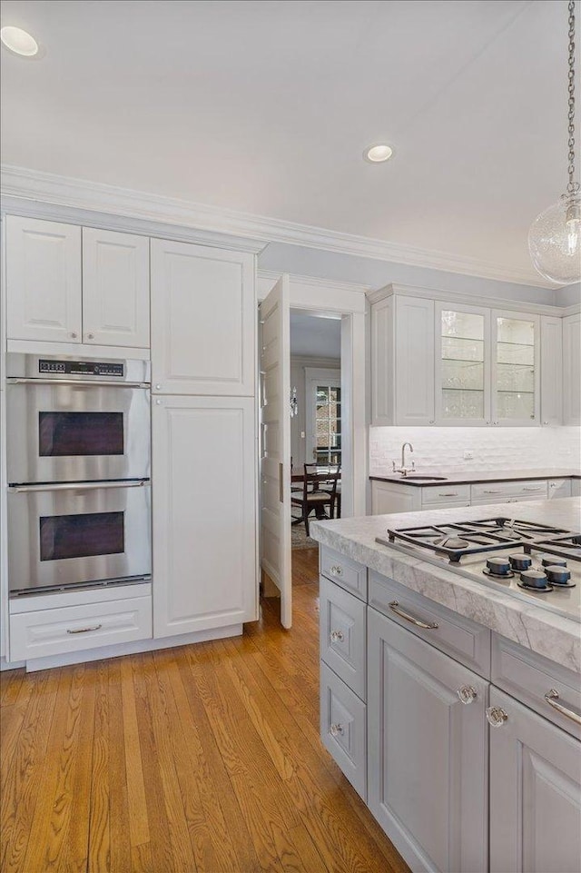 kitchen featuring stainless steel appliances, white cabinets, light countertops, light wood-type flooring, and crown molding