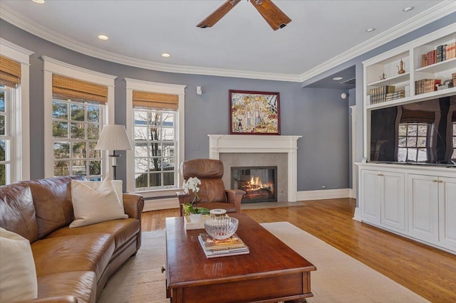 living room with ornamental molding, light wood-type flooring, a fireplace with flush hearth, and a ceiling fan