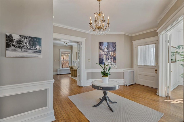 entrance foyer featuring wood finished floors, ornamental molding, wainscoting, radiator, and an inviting chandelier