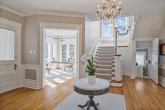 foyer entrance with a chandelier, a wainscoted wall, wood finished floors, ornamental molding, and stairway