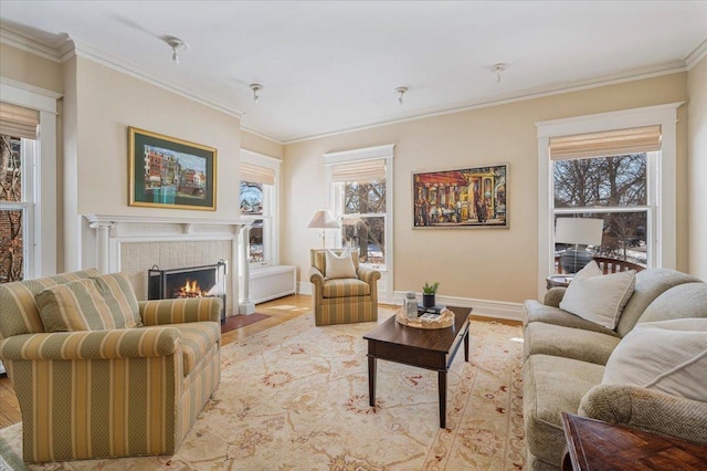 living area featuring ornamental molding, a warm lit fireplace, baseboards, and wood finished floors