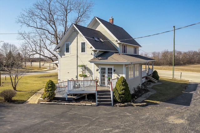 view of front of property with french doors, a wooden deck, roof with shingles, and a front yard