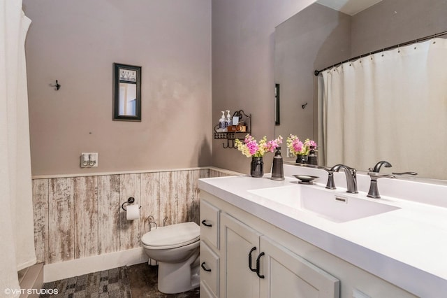 full bath with vanity, wooden walls, toilet, and a wainscoted wall