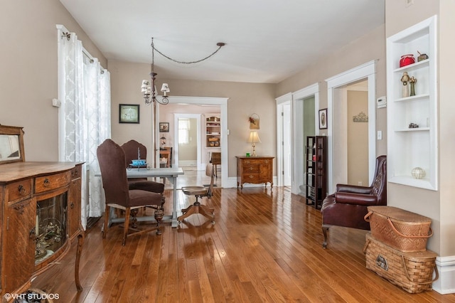 dining space featuring hardwood / wood-style floors, a notable chandelier, baseboards, and built in shelves