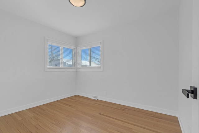 empty room featuring light wood finished floors, visible vents, and baseboards