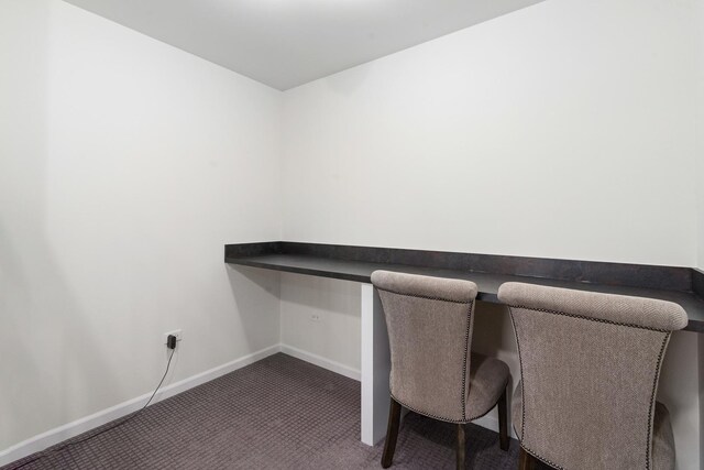 unfurnished office with built in study area, baseboards, and carpet flooring