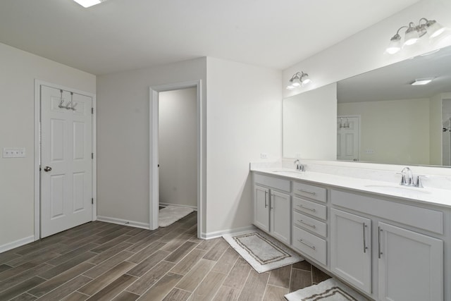 full bathroom with double vanity, a sink, baseboards, and wood finished floors