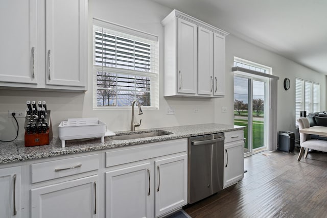 kitchen with stainless steel dishwasher, a sink, light stone counters, white cabinets, and dark wood-style floors