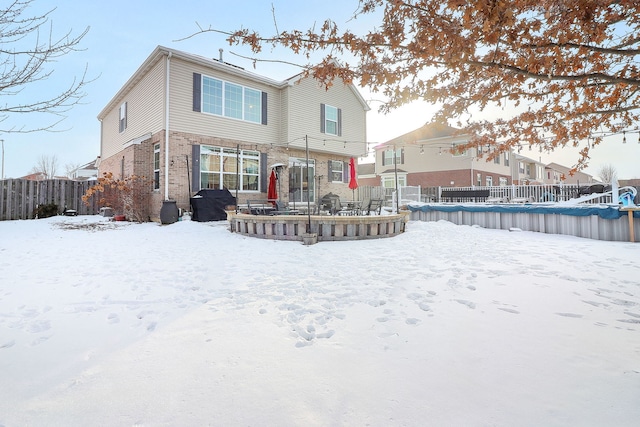 snow covered back of property with brick siding and fence