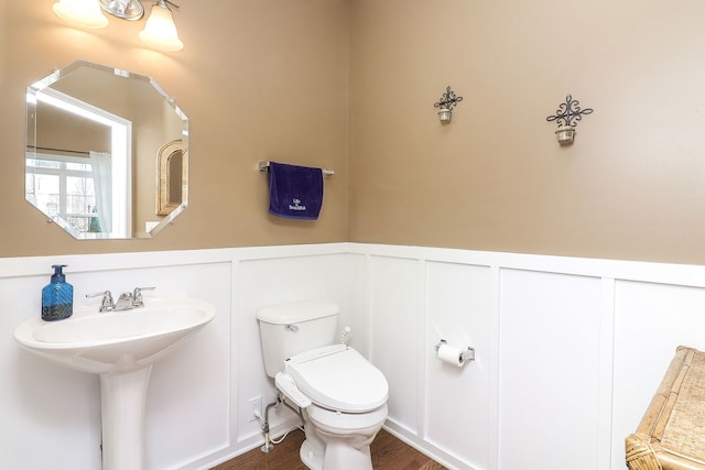 bathroom with a wainscoted wall, toilet, and wood finished floors