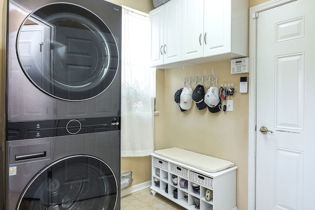 washroom featuring light tile patterned flooring, cabinet space, stacked washer and clothes dryer, and baseboards