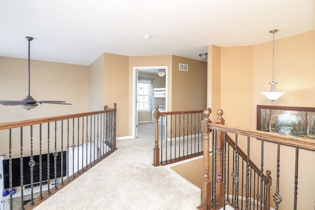 hall with carpet floors, baseboards, visible vents, and an upstairs landing