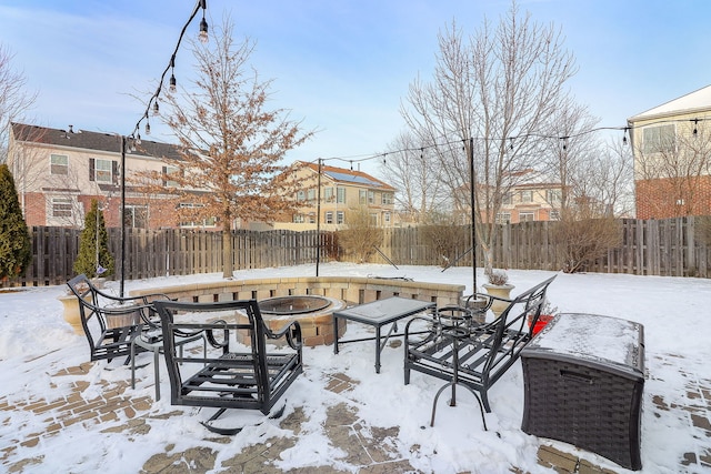 snow covered patio featuring an outdoor fire pit, a residential view, and fence