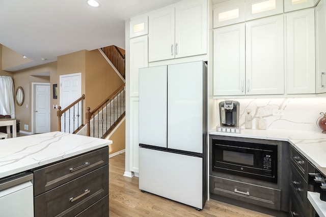 kitchen with black microwave, light stone counters, white cabinets, freestanding refrigerator, and glass insert cabinets