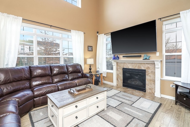 living area featuring light wood-style flooring, a high ceiling, baseboards, and a tiled fireplace