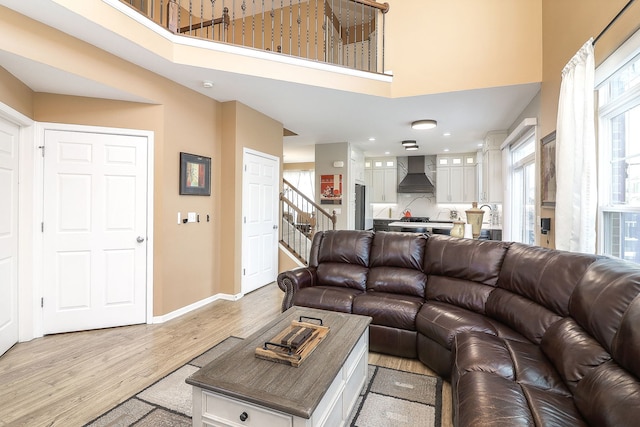 living room featuring light wood-type flooring, stairs, baseboards, and a towering ceiling