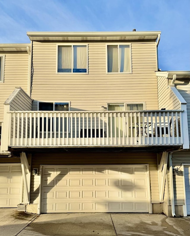 rear view of property with a balcony, concrete driveway, and an attached garage