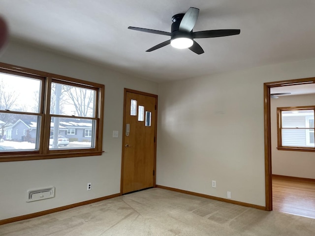 foyer entrance with a wealth of natural light, light carpet, and ceiling fan