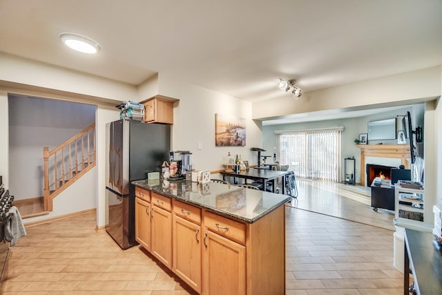 kitchen with stainless steel fridge, light brown cabinetry, and dark stone counters