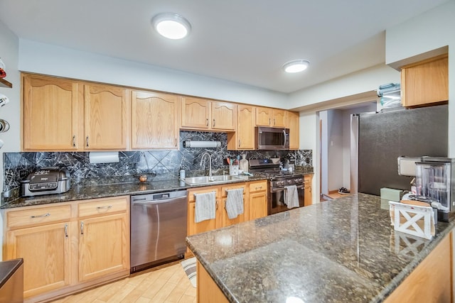 kitchen with sink, light wood-type flooring, dark stone countertops, stainless steel appliances, and decorative backsplash