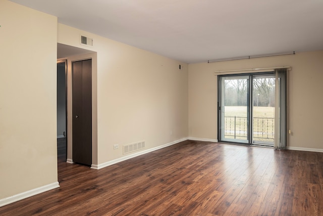 spare room featuring dark wood finished floors, visible vents, and baseboards