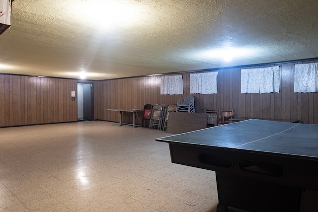 rec room featuring a textured ceiling, wooden walls, and tile patterned floors