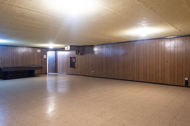 finished below grade area with a textured ceiling, light floors, and wooden walls