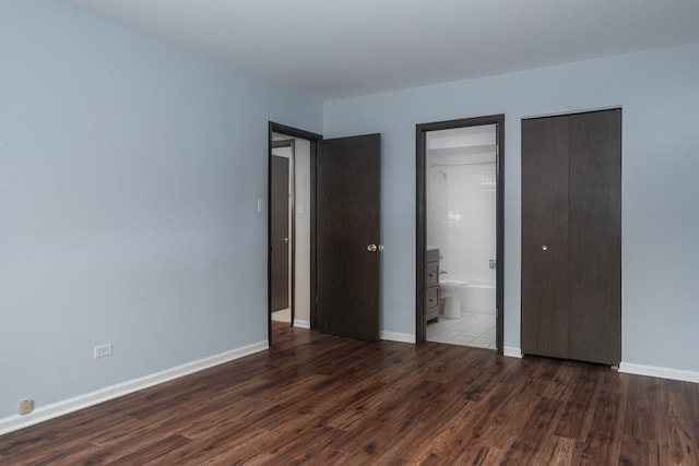 unfurnished bedroom with ensuite bathroom, wood finished floors, and baseboards