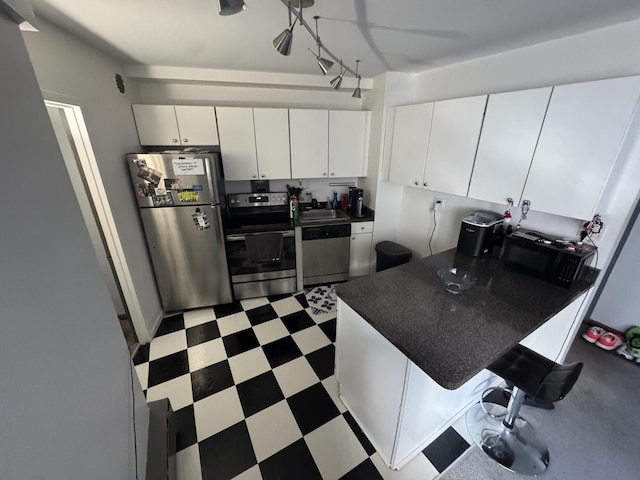 kitchen featuring stainless steel appliances, dark countertops, white cabinetry, a sink, and tile patterned floors