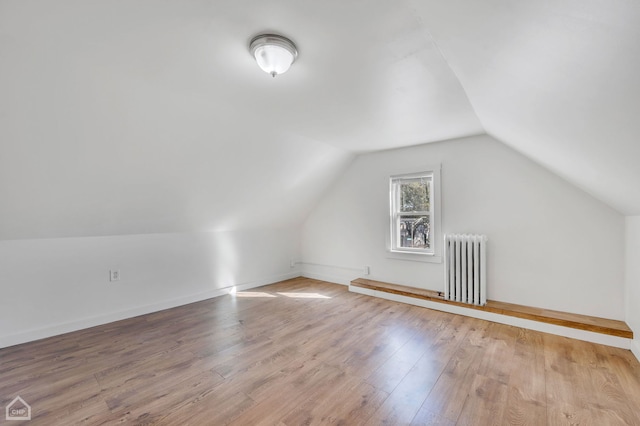 additional living space featuring radiator heating unit, light wood-type flooring, and vaulted ceiling