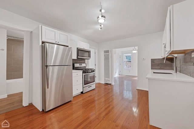 kitchen with white cabinetry, stainless steel appliances, light hardwood / wood-style floors, sink, and decorative backsplash