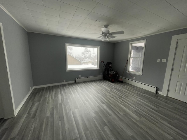 empty room with a baseboard heating unit, dark wood-type flooring, crown molding, and baseboards