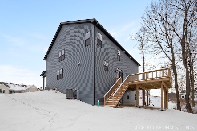 snow covered back of property with central air condition unit and a deck