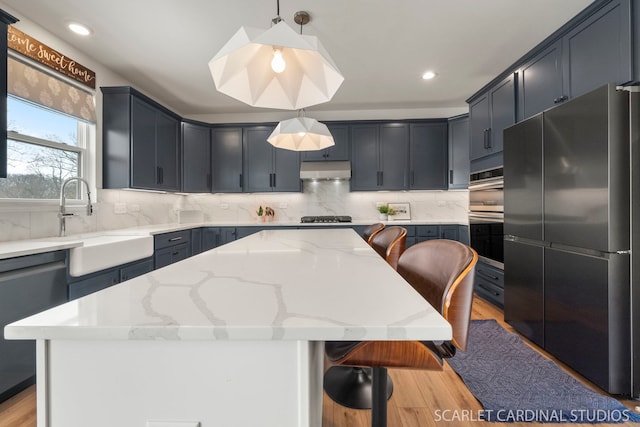 kitchen featuring appliances with stainless steel finishes, a kitchen breakfast bar, light stone counters, a kitchen island, and decorative light fixtures