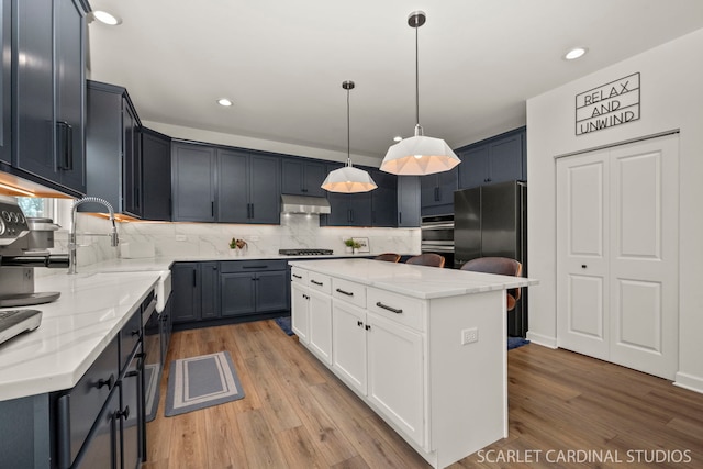 kitchen with black fridge, a center island, hanging light fixtures, light wood-type flooring, and gas cooktop