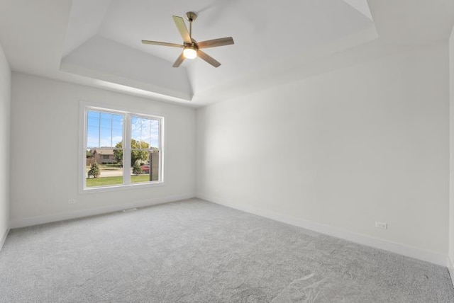 empty room featuring a raised ceiling, carpet flooring, and ceiling fan