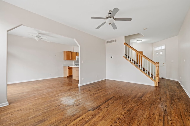 unfurnished living room featuring wood finished floors, stairway, baseboards, a ceiling fan, and visible vents