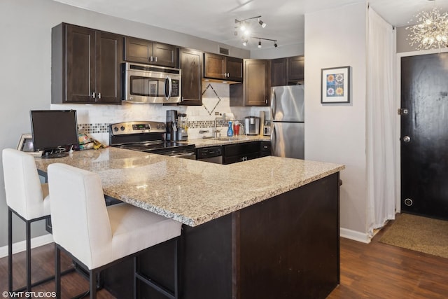 kitchen with a peninsula, dark brown cabinetry, appliances with stainless steel finishes, and a breakfast bar