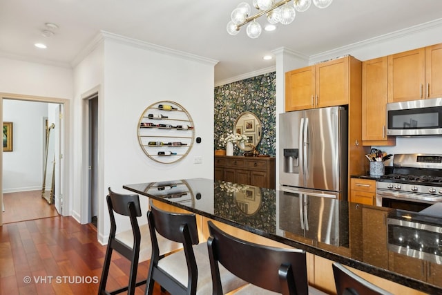 kitchen with appliances with stainless steel finishes, decorative light fixtures, ornamental molding, dark hardwood / wood-style floors, and dark stone countertops