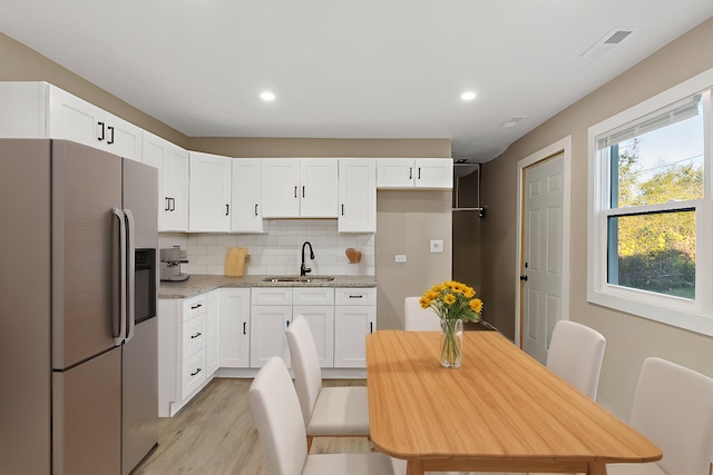 kitchen featuring white cabinetry, sink, stainless steel fridge, decorative backsplash, and light stone counters