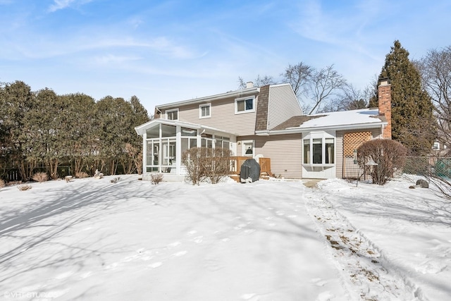 snow covered rear of property featuring fence, a chimney, and a sunroom